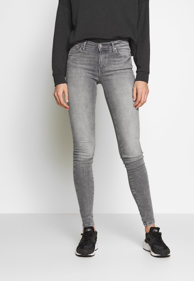 Vaqueros skinny grises de mezclilla con un diseño clásico de cinco bolsillos, lavado desvaído y un ajuste slim, combinados con zapatillas deportivas negras.
