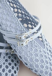 Sandales en plastique tissées bleu clair avec deux lanières réglables, ornées de boucles en métal, mettant en valeur un motif texturé tressé.