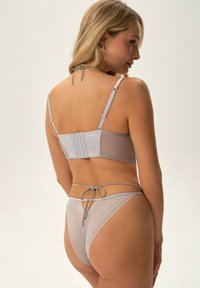 Jasnoszary zestaw bielizny składający się z dopasowanego biustonosza z regulowanymi ramiączkami i zapięciem na hak, w zestawie z pasującym stringami.