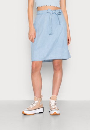Lichtblauwe denim rok met een gestrikte tailleband, met een rechte snit en subtiele textuur, gecombineerd met beige hoge sneakers.