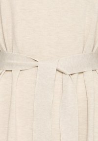 Tissu en maille beige clair avec une large ceinture nouée en un nœud lâche à la taille.