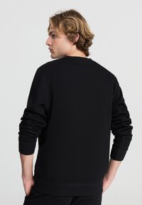 Felpa nera con maniche lunghe, colletto e polsini a coste, e una texture morbida. La vista posteriore evidenzia un design semplice senza grafiche.