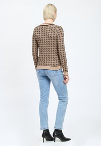Maglione a maglia marrone con motivo geometrico; design aderente con maniche lunghe e bordi a coste. Abbinato a jeans azzurri chiari e stivaletti neri alla caviglia.