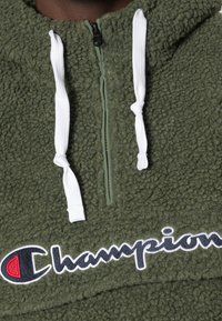 Felpa in pile verde oliva con chiusura a zip a un quarto, lacci bianchi e grande logo ricamato "Champion" in blu navy e rosso.