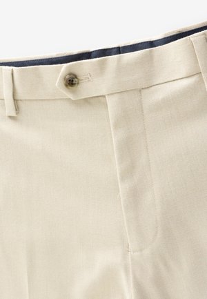 Pantalon beige avec fermeture à boutons, passants de ceinture, poche latérale et doublure intérieure de taille sombre.