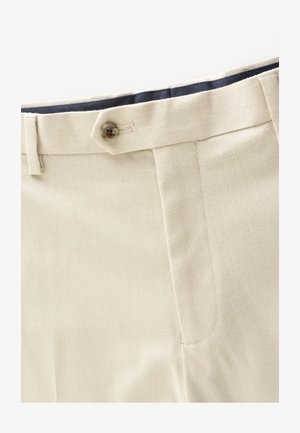 Pantalon beige avec fermeture à boutons, passants de ceinture, poche latérale et doublure intérieure de taille sombre.