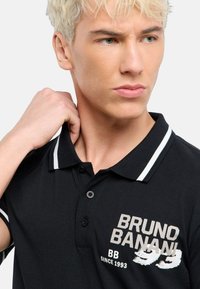 Sort polo skjorte med ribbet krave med hvide striber. Forsiden har "BRUNO BANANI!" logo og "BB SINCE 1993" i kontrastfarver.