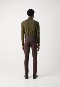 Μακρυμάνικο πλεκτό πόλο μπλουζάκι σε ελιά πράσινο χρώμα, συνδυασμένο με καφέ στενά παντελόνια, που συμπεριλαμβάνουν ζώνη, και μαύρα παπούτσια. Απλός σχεδιασμός και λείο υλικό.