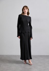 Top negru cu mânecă lungă, decolteu bateau, croi slim și tiv în două straturi, combinat cu o fustă lungă până la podea și sandale argintii.
