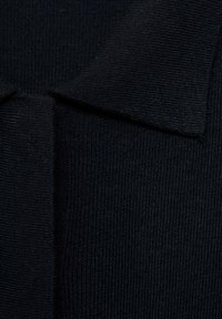 Czarny dzianinowy materiał o prążkowanej fakturze, z krótkim kołnierzem i plisą na guziki. Zdjęcie z bliska podkreśla materiał i szwy.