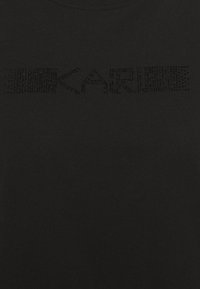 Černé bavlněné tričko s nápisem "KARL" v texturovaném designu z černých kamínků napříč hrudníkem. Hladká tkanina, kulatý výstřih.