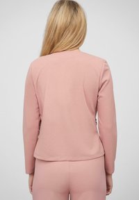 Hele roosa bleiser pikka varrukatega, sile tekstuur ja ümar tagumine äär, koos sobivate kitsaste pükstega, minimalistik disain.