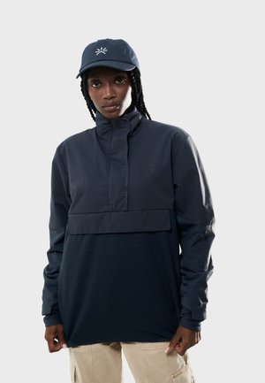 Veste pull marine avec col haut, poche avant, section inférieure texturée et casquette assortie arborant un logo blanc.