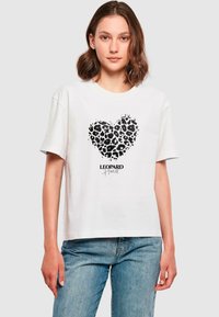 Valge lühikeste varrukatega T-särk, millel on musta leopardimustriga südame disain ja allpool tekst "LEOPARD Heart". Üksikasjalik sobivus.
