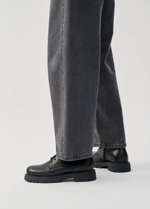 Zwarte leren schoenen met een ronde neus, vetersluiting en dikke rubberen zolen, gecombineerd met loszittende grijze spijkerbroeken.