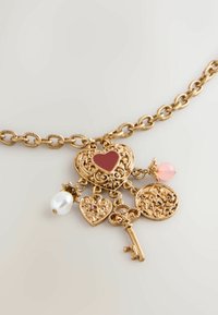 Goldfarbene Halskette mit herzförmigen Anhängern, einem Schlüssel und dekorativen Elementen, die rote, rosa und Perlenakzente aufweisen. Aufwändiges Design und Textur.