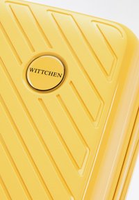 Valigia rigida gialla con superficie testurizzata, caratterizzata da scanalature diagonali e un logo circolare con "WITTCHEN" al centro.