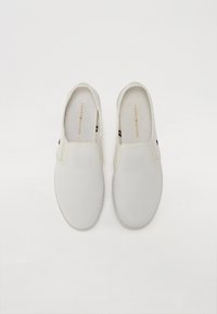 Fehér slip-on cipők sima vászon felsőrésszel, gumitalppal és egy kis színes akcentussal a saroknál. Arany logó a talpban.