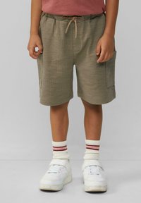 Khaki korte broek met een elastische tailleband en trekkoord, voorzien van twee zijzakken, gecombineerd met witte sneakers en rode gestreepte sokken.