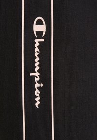 Tessuto nero con strisce verticali bianche. Logo "Champion" bianco in evidenza, visualizzato in corsivo lungo la striscia su un lato.