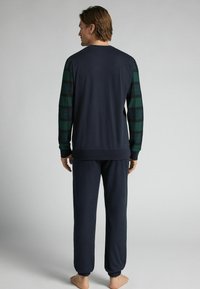 Námornícká pyžamová souprava obsahuje tmavý jednobarevný top s kostkovanými zelenými a černými rukávy a odpovídající jednobarevné kalhoty, vyrobené z měkké bavlněné látky.