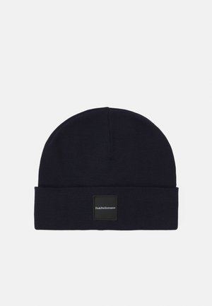 Dark navy beanie made of ribbed knit material. Features a folded cuff and a square black patch labeled "Peak Performance." Simple and functional design.