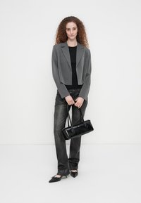 Κοντό γκρι σακάκι πάνω από μαύρο τοπ, συνδυασμένο με γκρι τζιν. Μαύρη τσάντα με λεία υφή και μαύρα μπαλαρίνες με μυτερή μύτη.