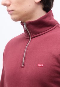 Νεαρό άτομο που φοράει ένα μπλεφούξια φούτερ Levi’s με φερμουάρ μέχρι τη μέση, το οποίο είναι μερικώς κλειστό και λογότυπο στο στήθος.