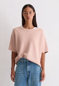 Różowy, oversize'owy sweter dzianinowy z szerokim wycięciem w łódkę, krótkimi rękawami i prążkowaną strukturą, w zestawie z jasnoniebieskimi jeansami z wysokim stanem.