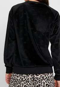 Top negro de manga larga, de terciopelo, con sutiles patrones semicirculares en relieve, combinado con una falda de estampado de leopardo.