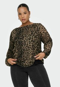 Blusa con stampa leopardata in tonalità terrose, materiale leggero, vestibilità ampia, scollatura a barca e maniche lunghe con polsini arricciati. Abbinata a jeans neri.