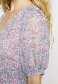 Vestido floral leve com padrões em rosa, verde e azul. Apresenta mangas bufantes e um design em V. Tecido transparente e texturizado.