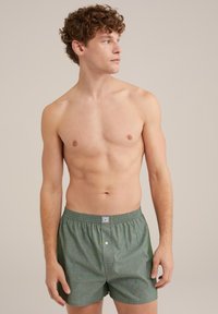 Žalios langelių rašto boxer šortai su elastingu juosmeniu ir vienu mygtuku. Lengvas audinys su glotnia tekstūra.