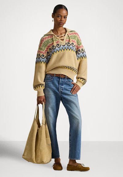 Μπεζ πλεκτό πουλόβερ με ζωντανά μοτίβα, φαρδιά μπλε τζιν και καφέ παπούτσια. Αξεσουάρ περιλαμβάνει μια ταμπά τσάντα χειρός. Μακριά μανίκια και γιακάς.