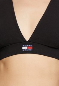 Černý v-neck bralet z hladkého materiálu, s logem ve středních červené, bílé a modré barvě umístěným pod prsy.