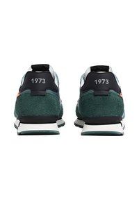 Sneaker in suede verde con accenti neri, caratterizzate dall'anno "1973" sul tallone e una suola intermedia bianca, che mostrano un design classico da corsa.