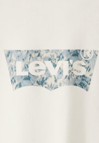 Tela blanca con un logotipo de Levi's en un patrón azul y blanco dentro de una forma de etiqueta roja característica. El diseño está centrado y es audaz.