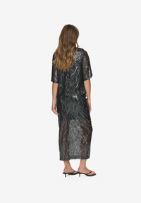 Ensemble en deux pièces noir à paillettes comprenant un haut court et ample à manches courtes et une longue jupe avec un motif abstrait, une texture transparente et une fente sur le côté.