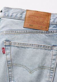 Jeans de mezclilla azul claro con un parche de cuero marrón etiquetado "LEVI STRAUSS & CO." que presenta detalles de costura y una etiqueta roja en el bolsillo.