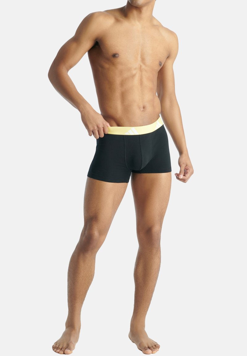 Svarta boxertrosor med en gul midjeband som har diagonala ränder, gjorda av mjukt, elastiskt material, designade för komfort och passform.