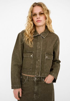 Olive green denim jacket with a cropped design, two front pockets, silver hardware, and visible stitching details. Textured fabric.