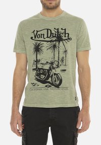 T-shirt en coton vert avec un graphisme de moto noire, des palmiers et le texte "Von Dutch". Manches courtes et design à col rond.