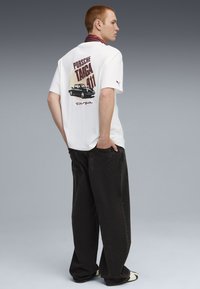 Hvid bomulds T-shirt med et vintage Porsche grafik på ryggen, parret med sorte vidde jeans. Skjorten har korte ærmer.