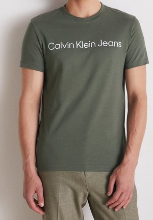 Olivengrünes T-Shirt mit kurzen Ärmeln aus weicher Baumwolle. Mit weißem "Calvin Klein Jeans"-Logo auf der Brust. Rundhalsausschnitt-Design.