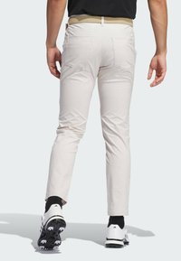 Pantalones de golf beige claro con un ajuste slim, con una cintura plana y dos bolsillos traseros, combinados con calcetines negros y zapatos de golf blancos.