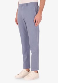 Pantaloni cropped azzurri realizzati in tessuto morbido, con tasche laterali, passanti per cintura e una chiusura con bottone singolo. Indossati con sneakers bianche.