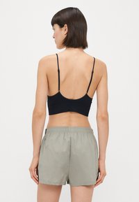 Crni bralet s podesivim trakama uparen s svijetlosivim šortsem. Fokus na jednostavnosti i udobnosti, s elastičnom vrstom.