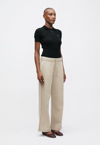 Čierny vrúbkovaný polo tričko, béžové široké tepláky s pružným pásom, hladká textúra, v kombinácii s vínovými plochými topánkami. Jednoduchý a pohodlný strih.