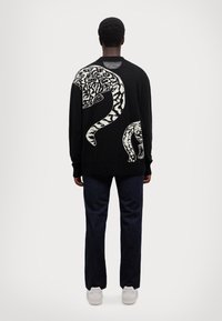 Maglione nero lavorato a maglia con un grande motivo di un serpente bianco sulla schiena. Abbinato a jeans blu scuro e sneakers bianche.