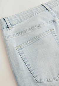 Blugi din denim de culoare albastru deschis, cu un buzunar posterior, cusături decorative, talie înaltă și textură fină.